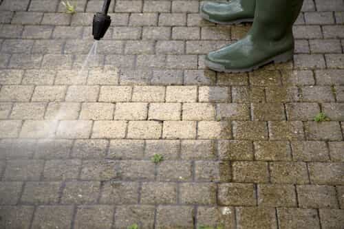 person using power washer on stone walkway
